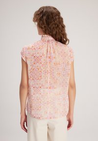 Kortebloes met bloemenmotief in pastelkleuren, met een geplooide halslijn, zachte stof en een herhalend geometrisch ontwerp in roze en oranje.
