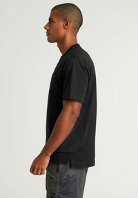 T-shirt nero a maniche corte in cotone, con scollo rotondo e tasche laterali; texture liscia e vestibilità comoda.