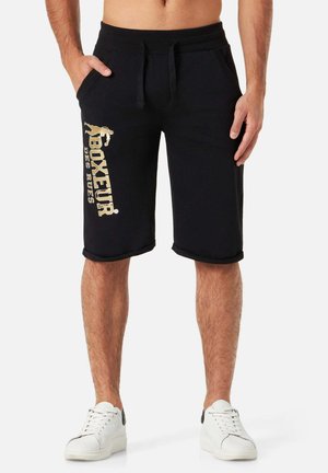 Schwarze Baumwollshorts mit einem elastischen Bund, seitlichen Taschen und einem goldfarbenen Logodruck am linken Bein. Umschläge am Saum.