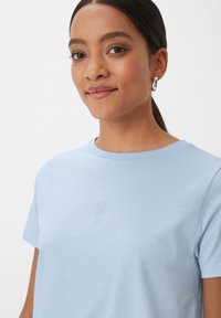 Lichtblauwe katoenen t-shirt met korte mouwen, voorzien van een subtiel logo in een lichtere tint op de borst, ronde halslijn, fijne textuur.