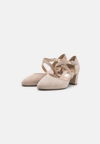 Chaussures à talons hauts en suede beige avec un bout pointu, une bride de cheville et un design croisé. Talon épais pour plus de stabilité et de confort.