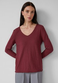 Langärmliges, burgunderfarbenes V-Ausschnitt-Shirt aus leichtem Stoff mit glatter Textur, das eine entspannte Passform und subtile seitliche Akzente aufweist.