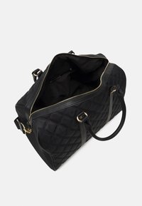 Černá prošívaná taška přes rameno s koženými detaily, zlatým zipem a dvojitými uchy. Vnitřek je podšitý černou látkou. Prostorné otevření.