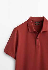 Polo manches courtes couleur rouille avec patte à deux boutons et col pointu, présenté sur fond blanc.