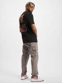 Black T-shirt with red lettering on the back, paired with light gray cargo pants and white sneakers with red accents.