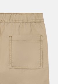Bézs rövidnadrág rugalmas derékrésszel, egyetlen hátulsó zsebbel, amely látható varrási részletekkel rendelkezik. Sima anyagtextúra.