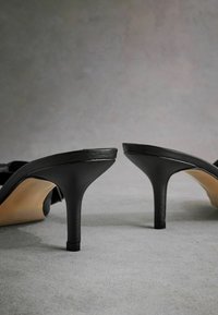 Sandales à talons hauts noires avec des brides en cuir lisse, design à bout ouvert, talon aiguille effilé et semelle intérieure beige.