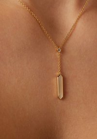Goldene Kettenhalskette mit einem langen, sechseckigen Anhänger mit glatter Oberfläche und einem kleinen Akzentstein nahe dem Verschluss.