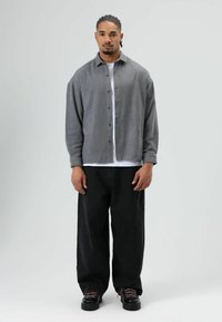 Grijs overhemd over een wit T-shirt, gecombineerd met losse zwarte spijkerbroeken en zwarte schoenen met roze veters. Eenvoudig, ontspannen pasvormontwerp.