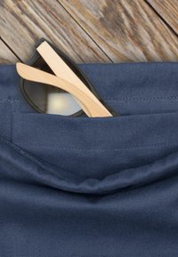 Sluneční brýle s černými skly a bambusovými rameny ležící v kapse tmavě modrého textilního předmětu s texturovaným povrchem a viditelným šitím.