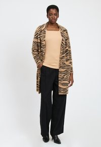 Brun og sort stribet cardigan i fluffy materiale, lagd ovenp�å en beige top, parret med sorte brede bukser og spidse sorte sko.