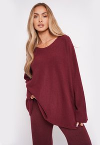 Przesadnie duży burgundowy sweter o szerokim dekolcie, z długimi rękawami i luźnym krojem. Miękka tekstura, w połączeniu z dopasowanymi spodniami w tym samym kolorze.