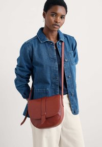 Borsa a tracolla in pelle marrone con patta e tracolla coordinata, caratterizzata da una superficie liscia e un design minimalista.