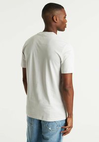 T-shirt di cotone grigio chiaro con maniche corte, collo rotondo e dettagli di cucitura discreti sul retro. Abbinato a jeans di denim blu.