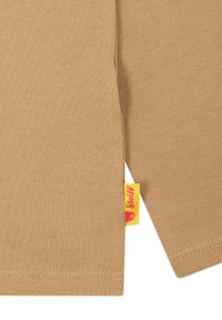 Beige Baumwolloberteil mit langen Ärmeln und gerippter Textur. Verfügt über ein gelbes Etikett mit einem Bärenlogo an der Seitennaht. Saum und Bündchen sind genäht.
