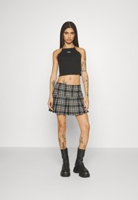 Black cropped tank top with a ribbed texture and a raw hem, paired with a plaid pleated mini skirt in black, white, and tan tones.