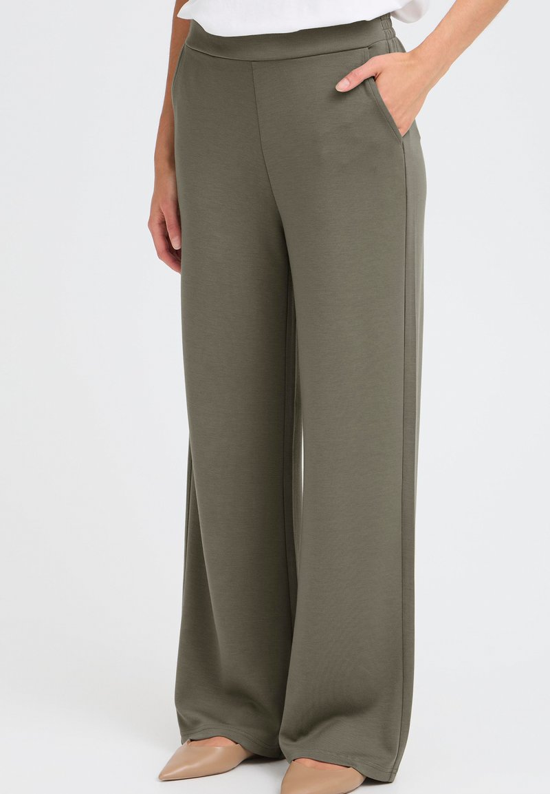 Pöyhiä lahkeet oliivinvihreänä, pehmeästä, teksturoidusta kankaasta. Korkea vyötärö ja sivutaskut, yhdistetty neutraaleihin korkokenkiin.