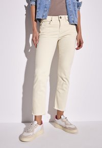 Krämfärgade jeans med raka ben och fransiga kanter, kombinerade med vita och beige sneakers med rosa detaljer. Ljus denimjacka ovanpå.