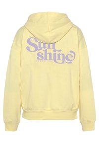 Žuta dukserica s opuštenim krojem. Na leđima se nalazi ljubičasti grafički natpis "Sunshine". Izrađena je od mekog, teksturiranog materijala.