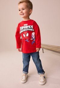 Czerwona koszulka z długim rękawem z grafiką Marvel's Spidey and Friends, zestawiona z dżinsami i białymi trampkami z niebieskimi akcentami.