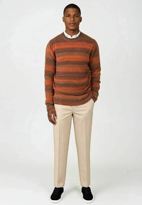 Oransje og grå stripete strikkegenser, rund hals, kombinert med beige bukser og svarte joggesko. Glatt tekstur, uformell design.