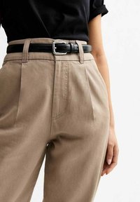 Beiga högmidjade byxor med kilar framtill, med ett svart läderbälte med en rektangulär silverspänne och en slät bomullstextur.