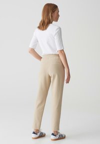 Beige tapse broek met een trekkoord in de taille, twee achterzakken, gestyled met een aansluitend wit topje en witte sneakers met blauwe accenten.