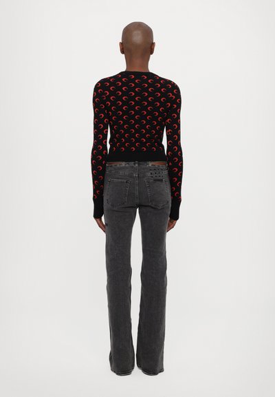 Černý pletený svetr s červeným vzorem půlměsíce, žebrovanými manžetami a lemem, v kombinaci se šedými rozšířenými džíny s klasickými zadními kapsami.