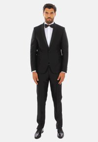 Tuxedo nero con revers in satin, camicia bianca e papillon nero. Design slim fit con finitura lucida; scarpe nere lucide completano il look.