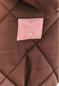 Hnedá prešívaná tkanina s ružovou našitou štítkom, na ktorom je grafika mihalníc, ikona globu a text o hviezdach a svetle.