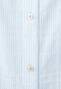 Close-up van lichtblauw-wit gestreepte stof met twee witte knopen genaaid op een verticale knopenbies.