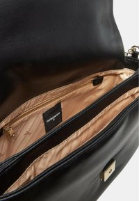 Borsa a tracolla in pelle nera con una texture liscia. L'interno presenta una tasca con zip dorata e un rivestimento in satin beige con un motivo. Etichetta del marchio visibile.