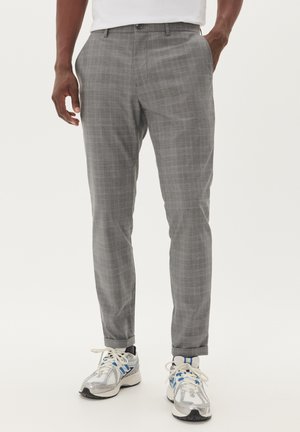 Pantalons à carreaux gris avec une coupe slim, présentant un devant plat, des poches latérales et des coutures décoratives. Portés avec des baskets grises.