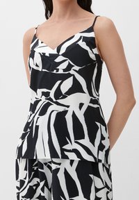 Haut sans manches noir et blanc avec un col en V, un motif feuille, et une texture plissée. Tissu léger avec une coupe fluide.