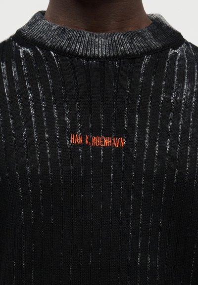 Μαύρο ριμπ πουλόβερ με μεταλλικές ρίγες, με στρογγυλή λαιμόκοψη. Το όνομα της μάρκας "HAN K.ØBENHAVN" είναι κεντημένο σε φωτεινό πορτοκαλί.