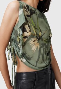 Haut sans manches vert floral avec fronces sur le côté et liens, porté avec un pantalon en cuir noir taille haute.