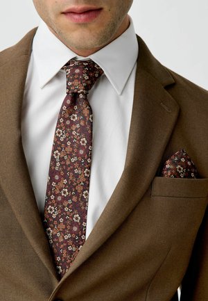 Sacou maro cu o cămașă albă, având o cravată florală închisă și un batista asortată. Cravata are flori mici albe și burdundii.