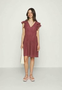 Φόρεμα σε χρώμα σμέουρου με V λαιμόκοψη, φουσκωτά μανίκια και σχέδιο με τρύπες. Συνδυάζεται με πλατφόρμες σε ανοιχτό ροζ και μια ελαφριά τσάντα.