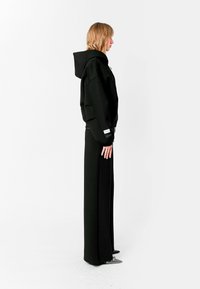 Sudadera negra de gran tamaño con una capucha grande, combinada con pantalones largos negros. Textura suave, diseño minimalista y detalles de abertura lateral.