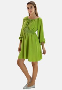 Vestido verde de hombros descubiertos con mangas largas abullonadas, cintura fruncida y detalle de botones. Tejido ligero con una textura suave.
