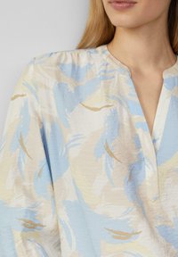 Luchtige blouse van zachte katoen met een blauw, crème en beige abstract patroon. Heeft een kleine kraag en korte geplooide mouwen.