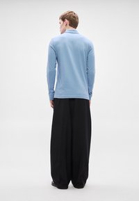 Šviesiai mėlyna ilgomis rankovėmis marškiniai su apykakle, derinami su laisvomis juodomis kelnėmis. Lygi tekstūra, minimalistinis dizainas ir laisvas siluetas.