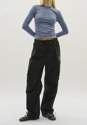 Lichtblauw geribd shirt met lange mouwen en contrasterende stiksels, gecombineerd met zwarte cargobroeken met trekkoord in de taille en zakken. Zwarte schoenen met studs.