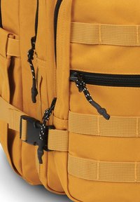 Mochila de tela amarilla que cuenta con múltiples bolsillos, cremalleras negras, correas ajustables y un broche lateral para un cierre seguro.