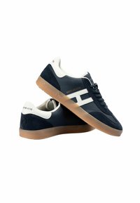 Zapatillas de ante azul marino con acentos blancos, que presentan una suela de goma, un diseño de cordones y una marca a lo largo del costado y el talón.