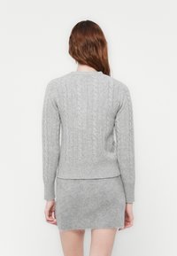 Maglione grigio a maglia con texture a trecce, maniche lunghe e orlo a costine. Abbinato a una gonna aderente grigia coordinata. Tessuto morbido e accogliente.