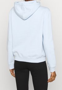 Vaalean sininen huppari, jossa on nyörin säädettävä huppu, resorikappaleet ja helma. Sileä tekstuuri, rento malli, ja takanäkymä, joka esittelee minimaalista muotoilua.