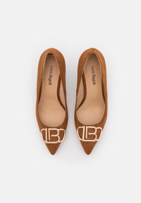 Bruna mocka ballerinor med spetsig tå som har en guldtonad logobuckle på framsidan, med en slät innerfoder och en minimalistisk design.