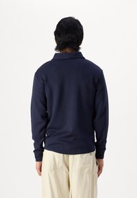Navy long-sleeve polo shirt with a textured finish and ribbed collar, paired with beige loose-fitting pants featuring back pockets.