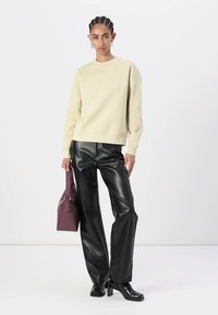 Sudadera beige, pantalones de pierna ancha de cuero sintético negro, sosteniendo un bolso de mano de color púrpura oscuro. Diseño simple, textura suave y silueta estructurada.